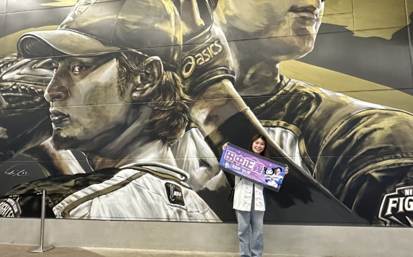 タワーイレブンの前で田中正義のタオルを持つ女性