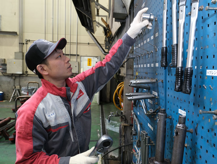 壁にかかっている工具を取るメカニックの男性